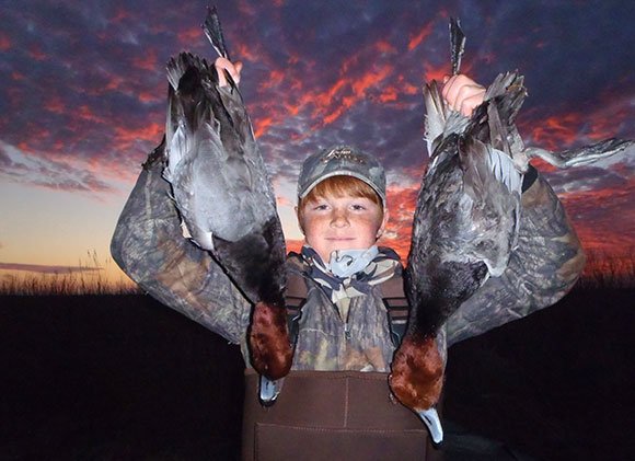 Young hunter holding up two redhead ducks at sunrise