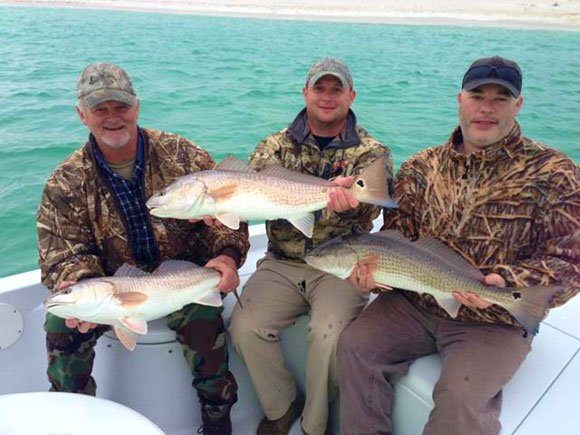 Three anglers holding redfish aboard the bay boat